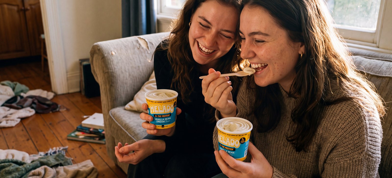 Two friends on a couch, one lifting a wooden spoon from a small Helado cup